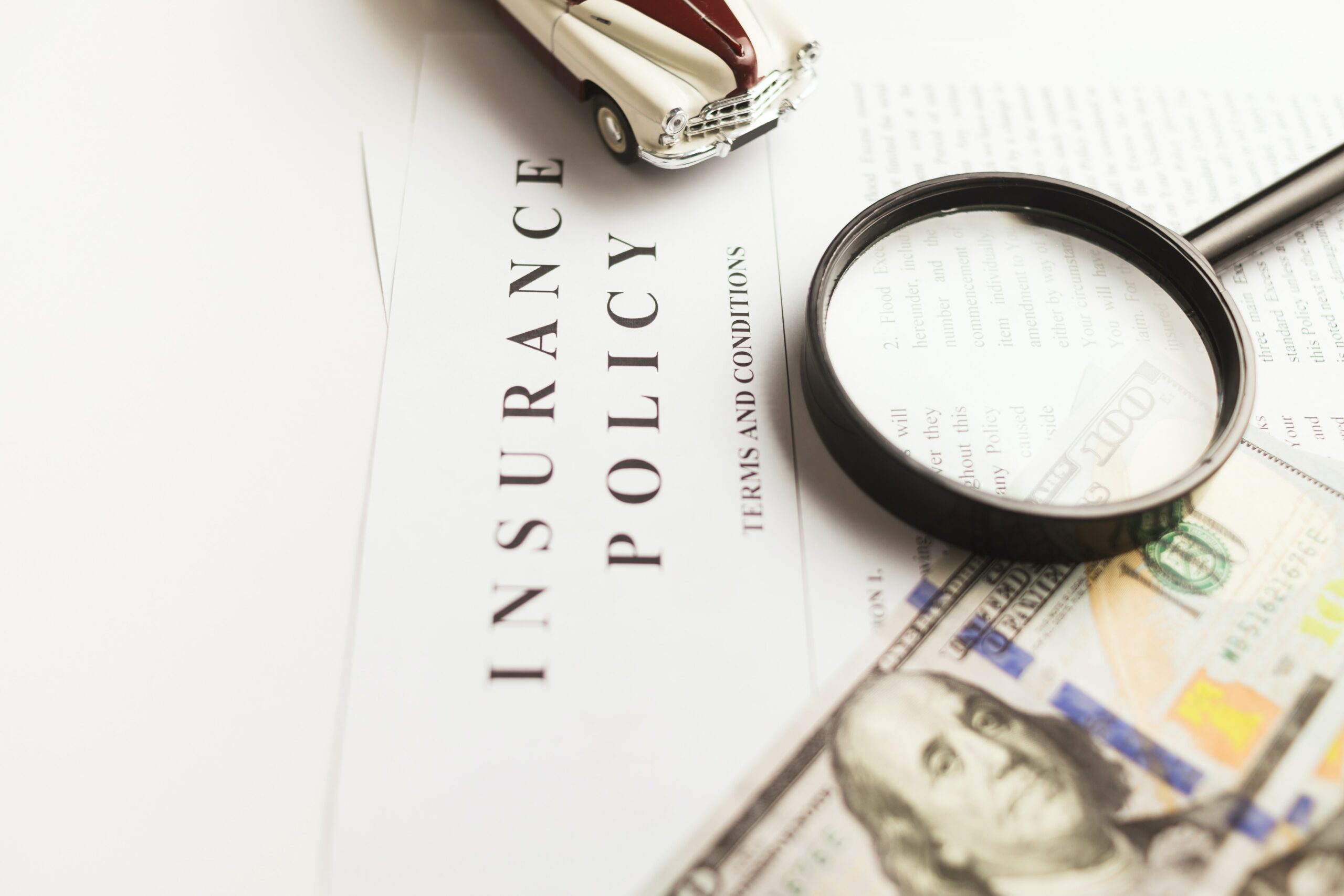 image of an insurance policy document with a magnifying glass and a hundred dollar bill.